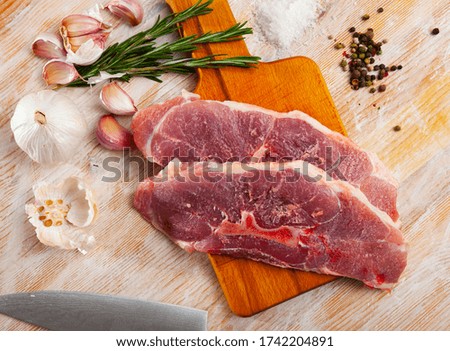 Close up of raw pork's  fillet shoulder with garlic and rosemary on wooden table, no people