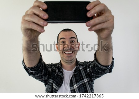  The main subject is out of focus or is not in focus, male stand white background take selfie blogger content creator hold smartphone