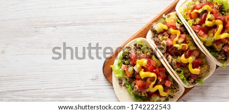 Homemade Cheeseburger Tacos on a rustic wooden board on a white wooden background, overhead view. Flat lay, top view, from above. Copy space.