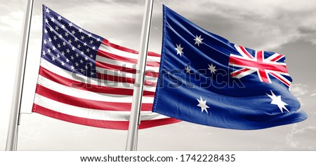 United States and Australia two flags on flagpoles and grey cloudy sky.