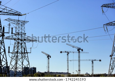 High-voltage power lines. High-voltage tower against the blue sky during the day in the city.high-voltage pole.Powerhouse. Construction cranes, home construction Royalty-Free Stock Photo #1742245193
