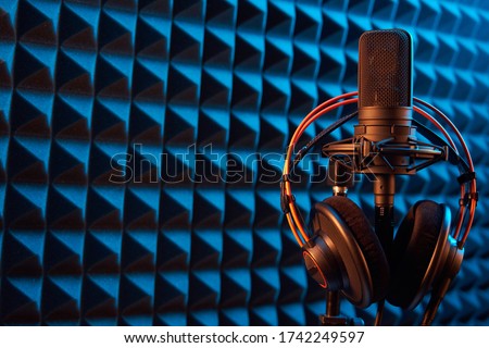 Studio condenser microphone with professional headphones on blue acoustic foam panel background