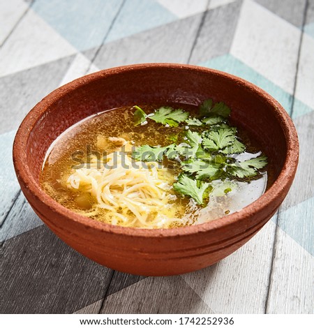 Classic chicken broth in brown pottery bowl. Delicious soup with noodles and poultry in ceramic deep plate on wooden table. Served chicken stock top view. Restaurant lunch meal course
