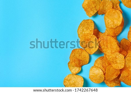Scattered spicy fried potato chips on blue background. Space for text. Top view