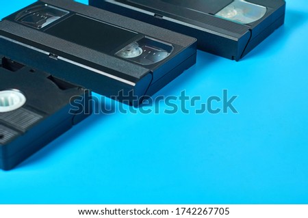 Row of three black old plastic vhs video cassettes near blank notepad lies on blue desk. Concept of 90s. Copy space