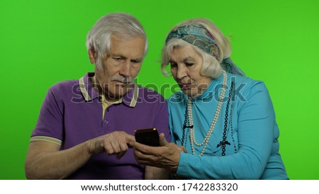 Elderly mature retired couple holding smartphone looking at mobile phone screen using social media app. Chroma key background. Senior old grandparents family having fun enjoy online shopping, news