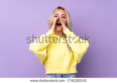Teenager girl wearing a yellow sweatshirt over isolated purple background shouting and announcing something