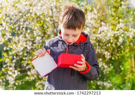 A teenage European boy received a gift in a red box. The child unpacked the package and is happy.