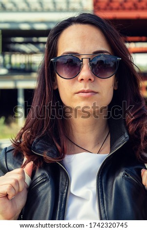 Portrait of a young woman in a leather jacket and sunglasses.