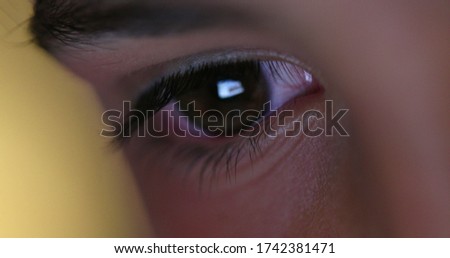 
Close-up of child eyes staring at screen. Macro red eye looking at blue light at night