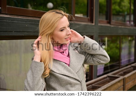 Horizontal portrait in profile of a caucasian blonde woman in coat. A model stands outdoors against the background of a wall of a building in the city.