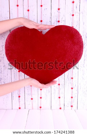 Hands holding big red heart on wooden background