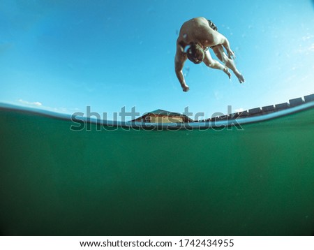 man jumping from wooden pier in lake water