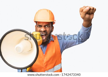 Emotional Black Construction Worker Shouting In Megaphone Looking At Camera And Shaking Fist Over White Background. Studio Shot Royalty-Free Stock Photo #1742473340