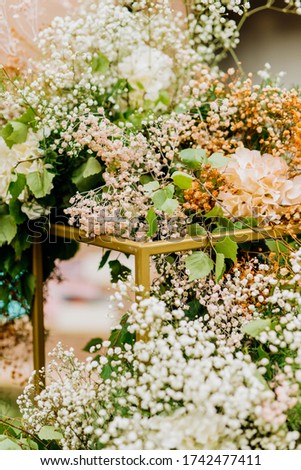 The metal structure of the wedding arch in the shape of a cube is decorated with greenery and hydrangea flowers with gypsophila.