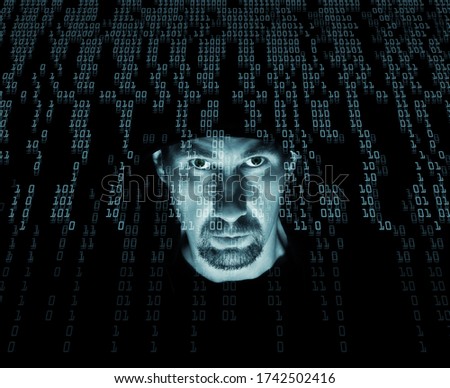 A man in a hood in a stream of binary code. Cyber criminal and data stream with light blue filter background.