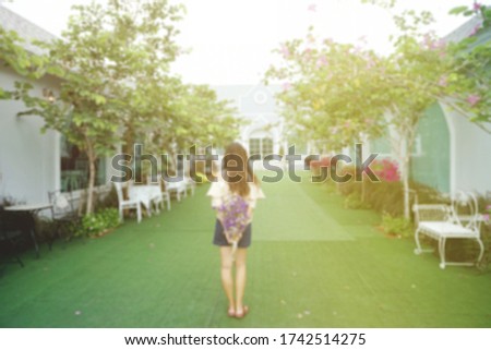 blurred image of long hair girl standing on grass field walk path holding flower bouquet in the back, romantic love concept, abstract background