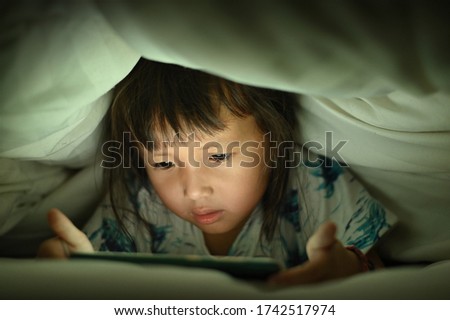 Child are watching video smart phone under the blanket on bed at night time light flashes reflected from the screen,children using games with addiction and cartoon concept