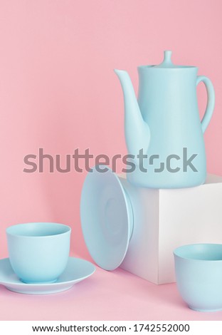 minimalism concept with light pastel colored blue cups and plate and teapot with white paper cubs on pink background. 