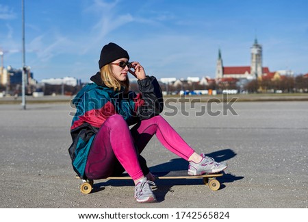 A pretty young blond woman with skateboard outdoors, sunny day.
