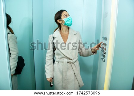 brunette girl with coat takes the elevator wearing the protective face mask