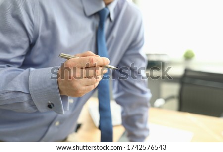 Close-up of businessman holding silver pen. Man in stylish blue costume in office. Successful employee signing contract. Business growth and economy concept