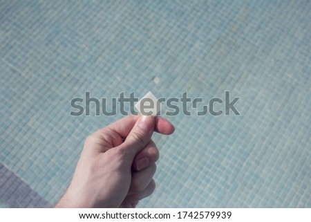 Close-up of white tile holding by a hand on the empty stoneware pool with a little hole in the background. Empty pool.