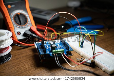 Close up shot of a micro controller (nucleo) connected with wires to a bread board tools and wiring in the background on a wooden table. Photo was taken during shelter in place order working from home Royalty-Free Stock Photo #1742585834