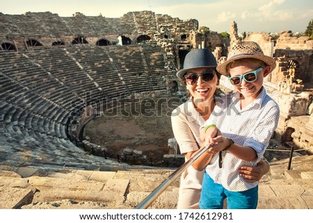 Mother with son smiling to camera taking a selfie photo in antique theatre using a selfie stick. Traveling around the world with kids concept image.