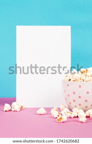 Fresh popcorn in a white pink bowl on pink and blue background with the blank paper page