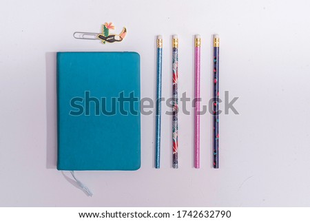 blue notebook with pencils and a paper clip with a bird on a white background
