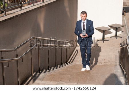 Businessman talking on cell phone against the building with a glass facade. Confident manager with cellphone walking on stairs holding cup of coffee