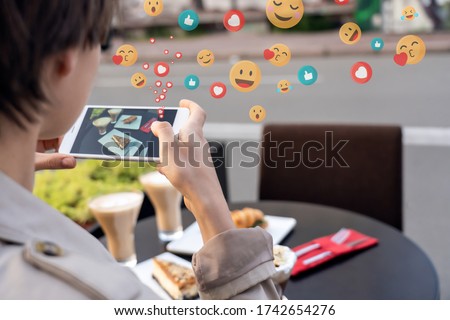Female blogger influencer hold phone take food mobile photo on phone sit at cafe table. Girl vlogger shoot social media instagram post on smartphone get many likes emoji over shoulder closeup view. Royalty-Free Stock Photo #1742654276