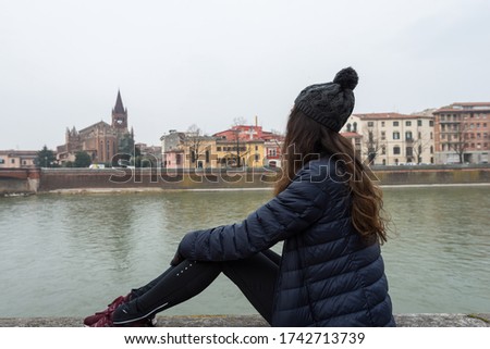 Horizontal picture of brunette woman looking to Adige River during cold day in Verona, one of the attractions of Italy