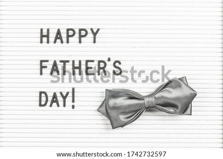 Happy Father's Day text on letter board with silver bow tie on white textured surface. Minimal text poster or web banner. Copy space. Father's Day Sale mockup