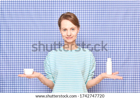 Blond girl with anti-acne skincare product on face is holding cosmetic bottle and jar on open hand palms, standing over shower curtain background. Care for imperfect acne-prone skin. Beauty concept
