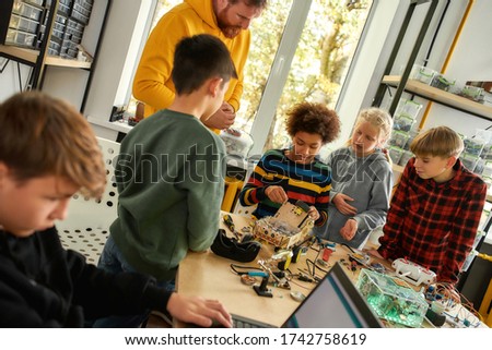 Young technicians building a robot vehicle together with a male teacher at a stem robotics class. Inventions and creativity for kids. Tinkering, educational activities concept. Dutch angle