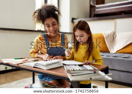 Caucasian little girl spending time with african american baby sitter. They are drawing, learning to write letters, reading a book. Children education, leisure activities, babysitting concept Royalty-Free Stock Photo #1742758856