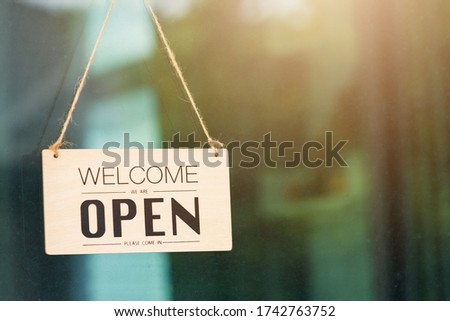 Close up of WELCOME WE ARE OPEN PLEASE COME IN notice sign wood board label hanging through glass door front shop, Business open back to new normal after coronavirus disease concept