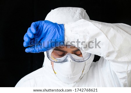 COVID-19. Exhausted Doctor, in personal protective equipment, worried as the coronavirus infected cases and death tolls rises. Emotional stress of health workers . Royalty-Free Stock Photo #1742768621