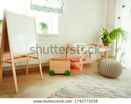 Kindergarten room with easel chair and table for painting. children  space. empty white desk at kindergarten. no people. modern interior. sunlight and plants on windowsill
