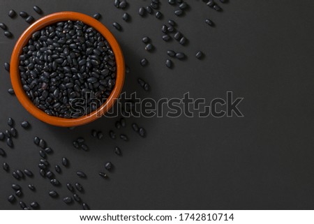 Top view of a bowl with black beans on a black background.