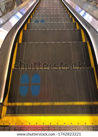 Infection control against Coronavirus pandemic. Foot-shaped-markings on a moving escalator. One should stand on the mark to do Social distancing.