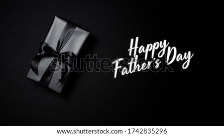 Happy Father's Day background concept with top view of black gift box with black ribbons isolated on black background.