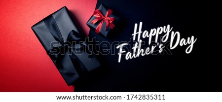 Happy Father's Day background concept with top view of black gift box with red and black ribbons isolated on black and red background.
