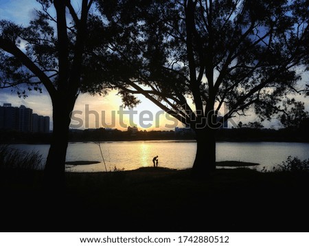 father and his child are enjoying the beautiful moment by watching the sunset near the lake 