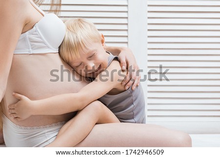 Little boy hugging his stomach of pregnant mother and laughs. young pregnant woman and the eldest son.