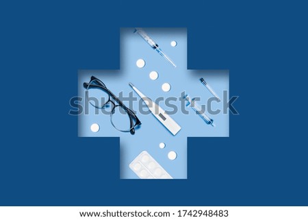 Medical classic blue background with different accessories: syringe, tablets, thermometer, glasses lying in a carved medical cross.