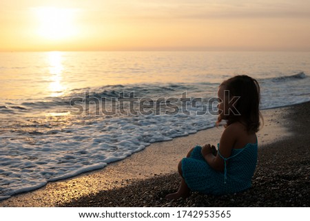 child a girl in a blue knitted dress by the sea walks and watches the sunset. Turkey