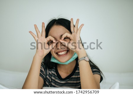 Girl wearing sanitation mask, striped shirt, and hand symbol, okay